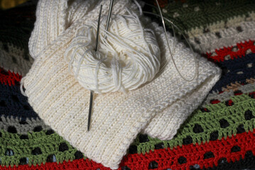 Knitting with needles with white threads, against the background of a knitted colored background