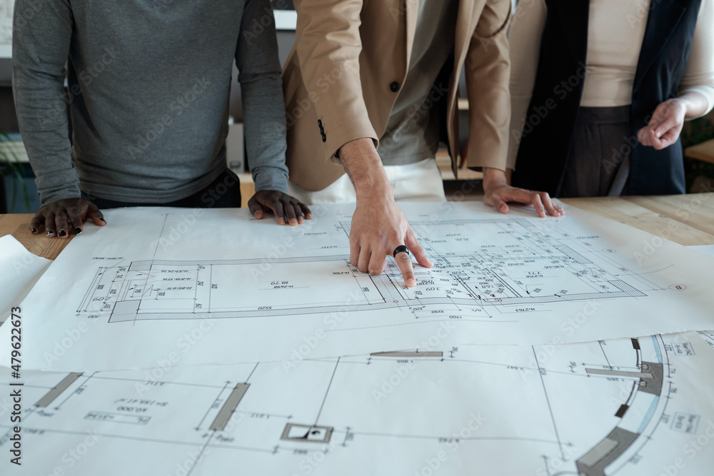 Poster hand of young contemporary engineer pointing at sketch while explaining it to intercultural male and
