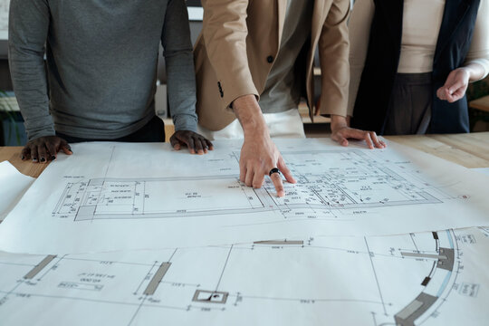 Hand of young contemporary engineer pointing at sketch while explaining it to intercultural male and female colleagues