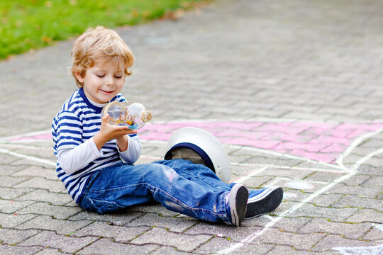 Little kid boy as pirate on ship or sailingboat picture painting with colorful chalks on asphalt. Creative leisure for children outdoors in summer. Child with captain hat and binoculars.