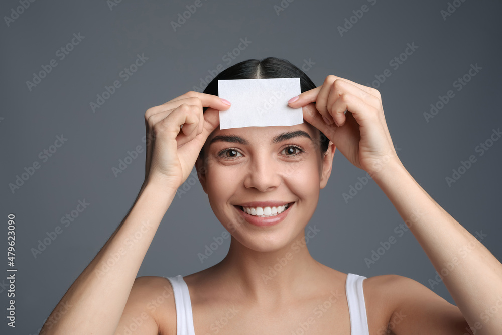 Wall mural Beautiful woman using mattifying wipe on grey background