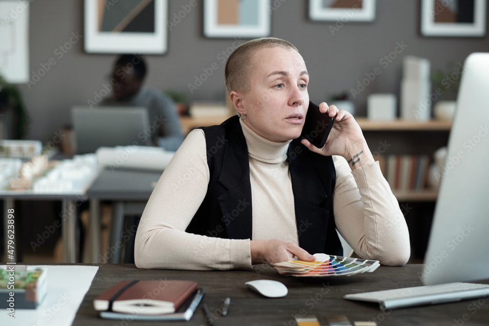 Poster Contemporary female designer speaking on mobile phone while sitting in front of computer monitor and consulting clients