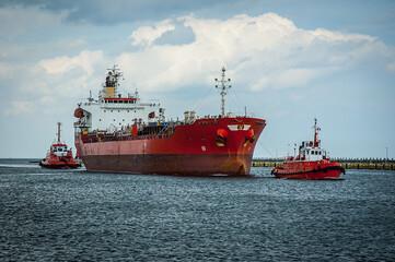 czerwony statek handlowy wchodzący do portu - obrazy, fototapety, plakaty