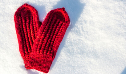 Red mittens in the form of a heart on white snow in winter