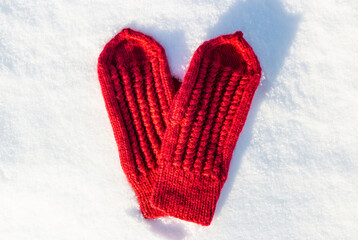 Red mittens in the form of a heart on white snow in winter