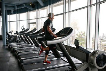 Elderly man running on treadmill in gym