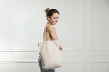 Happy young woman with blank eco friendly bag near white wall