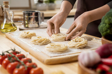 Hands of young creative woman preparing italian pasta on wooden board while standing by kitchen table
