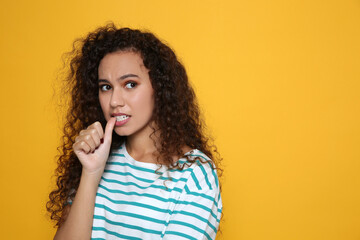 Fototapeta na wymiar African-American woman biting her nails on yellow background. Space for text