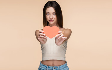 smiling young woman in crop top with bare shoulders holding red paper heart isolated on beige