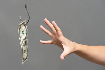Hand trying to catch a dollar on the fishing hook close up. Financial trap concept.