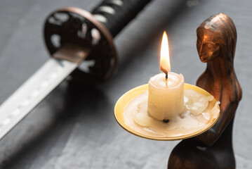 Burning candle on the samurai sword background close up.