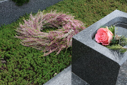 Herbstkranz aus roten und weißen Erikabüscheln als Dekoration zu Allerheiligen auf einem Familiengrab neben einer Rose im Weihwasserbehälter, Herbstschmuck auf einer Grabstätte, Gedenken, Floristik