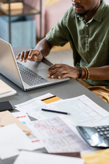 Hands of young African male economist working in front of laptop while sitting by table with financial documents