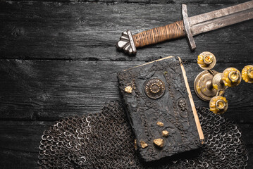 Ancient book and medieval weapon on the table flat lay background. Knight story book concept.