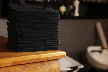 Fototapeta na wymiar stacked black bathroom towels on a wooden table and brick wall background. spa salon, barbershop