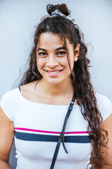 Portrait of a young woman in the summer in the city - Millennial looks at the camera and smiles friendly in front of a gray wall - Copy space - 479627646
