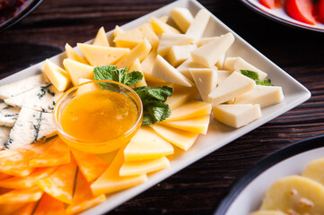 Slicing of various cheeses, cheeses lie on a white plate with honey on a wooden table.
