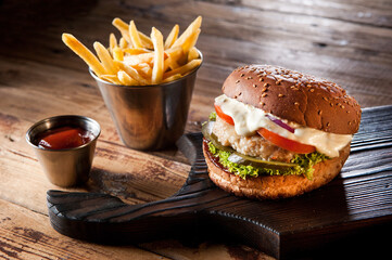 The meat burger lies on the board, next to the potatoes and ketchup is poured into the container