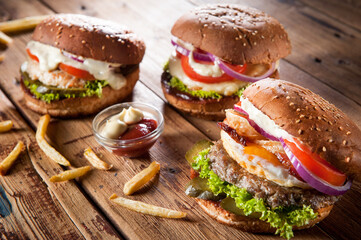 three meats burgers lies on the board, potatoes are scattered nearby and ketchup is poured into the container