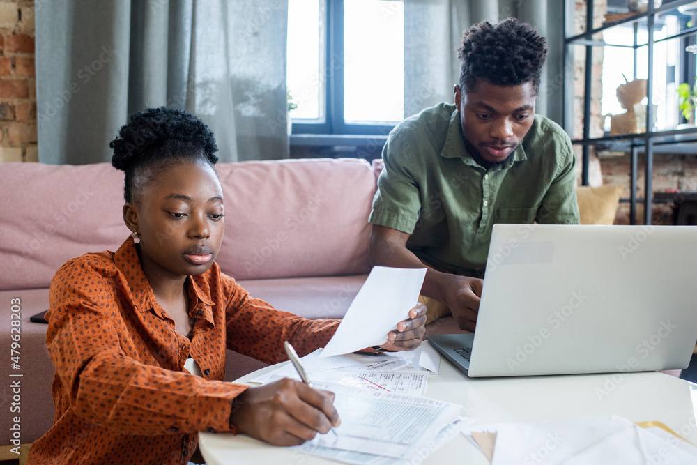 Poster Two young African colleagues working with financial papers and computer data while sitting by white round table