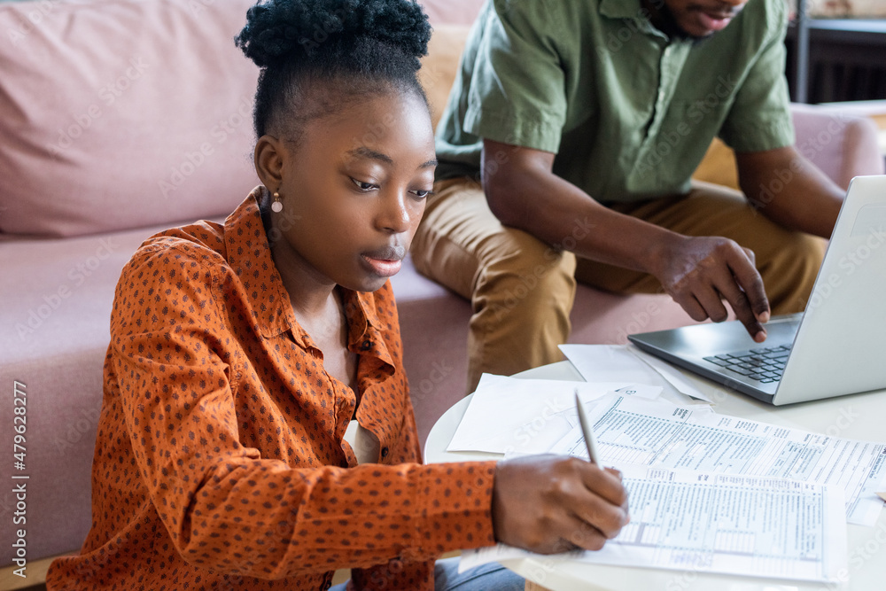 Aufkleber young serious african woman making notes in financial document while sitting against man networking 