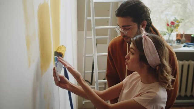 Young couple arguing, man and woman painting walls in yellow and quarreling, making overhaul. Husband and wife doing renovating together. Interior design, new apartment. Family problems. 
