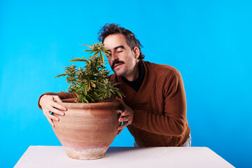 a man smells the flower of a cannabis plant on a blue background
