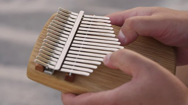 Closeup hands holding and play Kalimba Mbira or thumb piano. African musical instrument. Kalimba made from wooden board with metal, play on hands and plucking tunes with thumbs. selective focus
