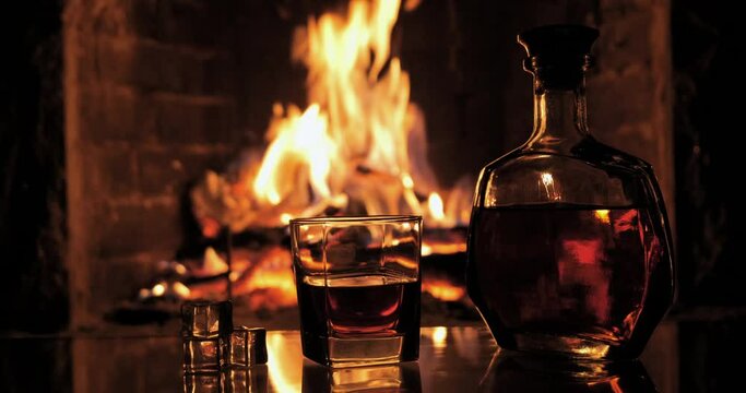 Bottle and glass with whiskey or cognac on the background of fire in the fireplace