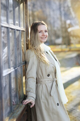 Fototapeta premium young blond slavic woman with long hair wearing trench coat close up street portrait on city park background