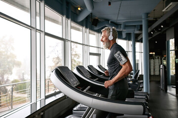 Fototapeta Senior man in gray t-shirt and white headphones in gym obraz