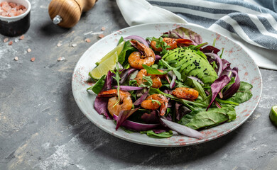 Green salad with avocado and shrimps salad. Seafood concept. Tasty veg mixed leaves, grilled prawn shrimps. Delicious breakfast or snack on a gray background, top view