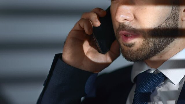 Closeup business man talking smartphone corruption crime bribe at night office jalousie shadow