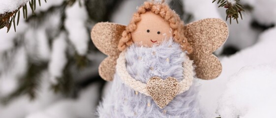 A soft textile doll with golden heart in hands sitting on the snow. Valentine’s Day, love, Merry Christmas, New Year concept. Banner.