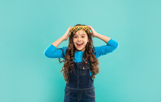 laughing child with curly hair in queen crown on blue background, happiness