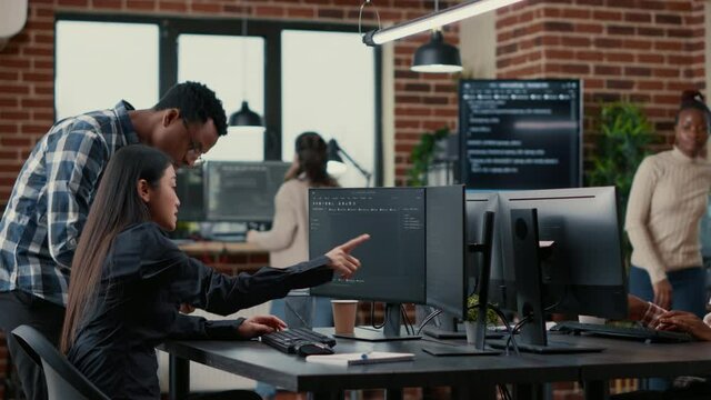 Mixed team of software developers analyzing source code pointing at screens comparing algorithm with user interface on digital tablet. Programmers working on coding group project sitting at desk.