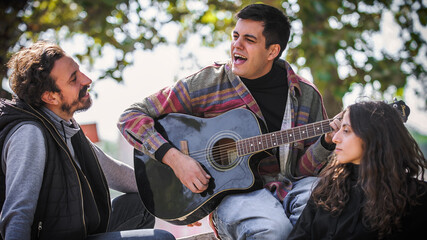 Friends play guitar and singing together while sitting on bench