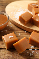 Yummy caramel candies and sea salt on wooden table, closeup