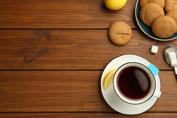 Flat lay composition with tea bag in ceramic cup of hot water, cookies and lemon on wooden table. Space for text