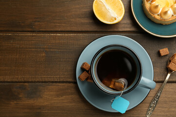 Tea bag in ceramic cup of hot water and sugar cubes on wooden table, flat lay. Space for text