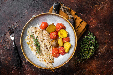 Roasted Pollock fish fillet in plate with garnish tomato and potato. Dark background. Top view - obrazy, fototapety, plakaty
