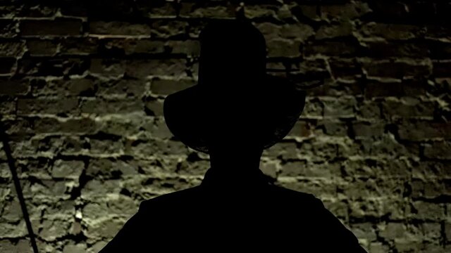 The silhouette of a man puts on a hat and against the background of a brick wall. Close up
