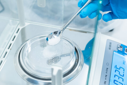 Close up scientist hands in rubber gloves use metal spatula for weighing white powder of the substance using digital balances. Preparation to clinical or pharmaceutical analysis