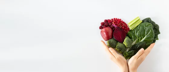 Foto op Aluminium Colorful heart shape from various fruits and vegetables with human hands holding it isolated on white background. Healthy plant-based food concept. Copy space for text. Top view. Love for fresh food. © Marinela