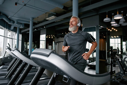 Active senior man jogging on treadmill in sports center