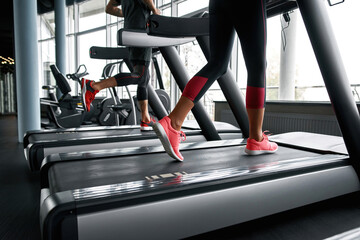 Fototapeta na wymiar Lower legs part of fitness woman and man running on running machine