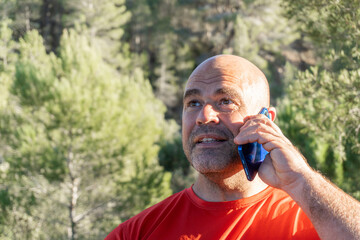 Middle-aged Caucasian man talking on the phone in nature.