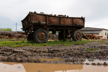 Obraz premium Old abandoned rusty tractor trailer. Stands on a green lawn in a muddy puddle.