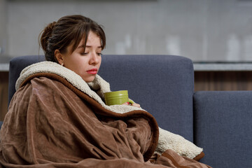 Woman with a cup of tea, covered with a blanket, resting on her armchair for being ill